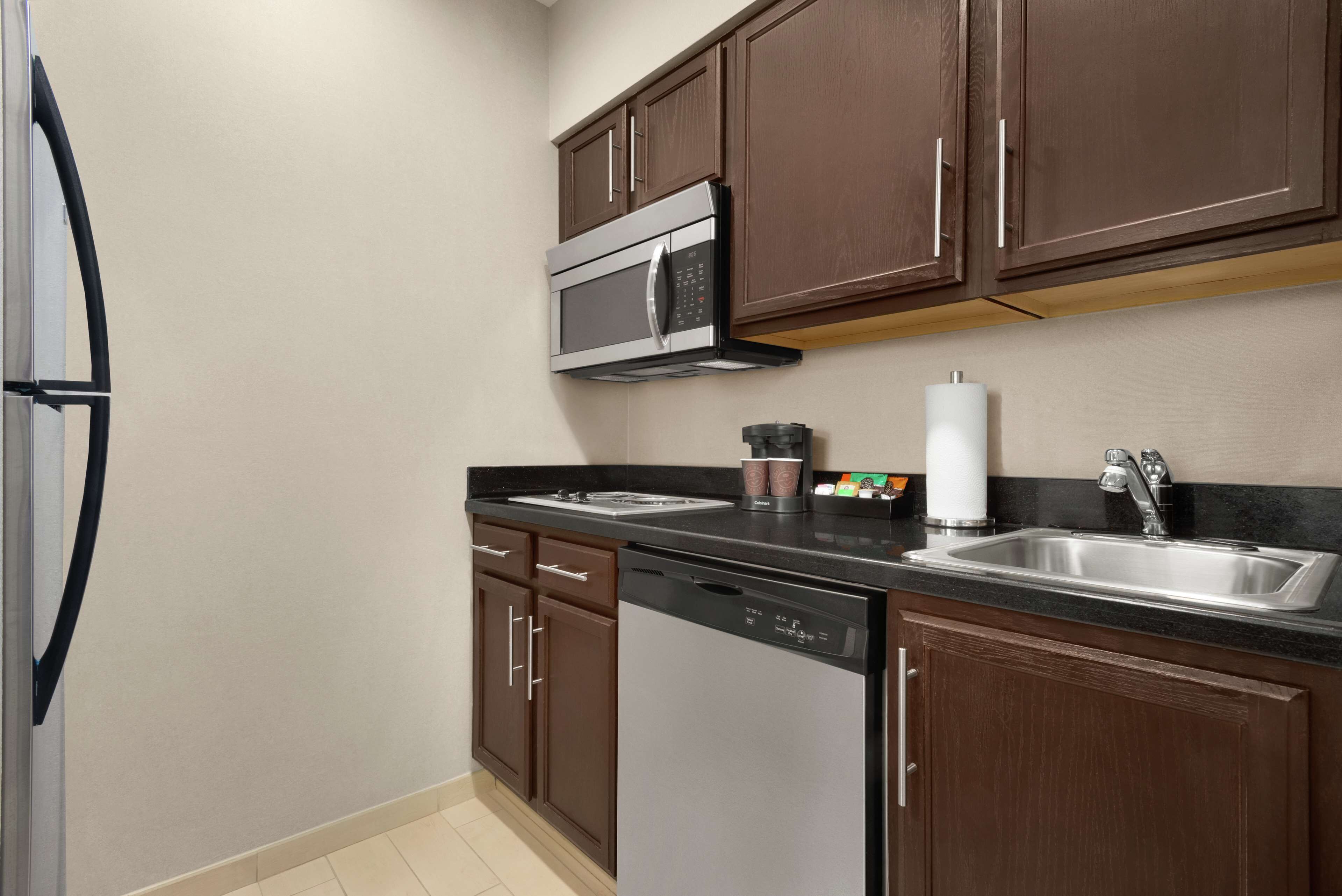 A kitchen with dark brown cabinets, a stainless steel microwave, a dishwasher, and a sink with a faucet.