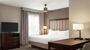 A hotel room with a bed, a desk, a television, a ceiling fan, and a window with curtains. - Homewood Suites Fort Wayne (Fort Wayne)
