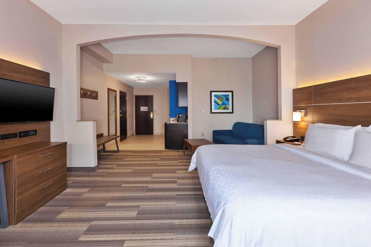 Une chambre d’hôtel dotée d’un grand lit, d’un téléviseur à écran plat, d’un bureau avec un ordinateur et d’un coin salon comprenant une chaise et une lampe.