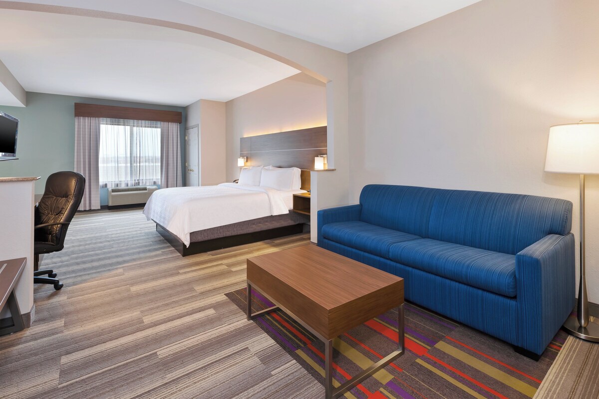 Une chambre d’hôtel avec un lit, un canapé bleu, une table basse en bois, un bureau avec une chaise et un téléviseur.
