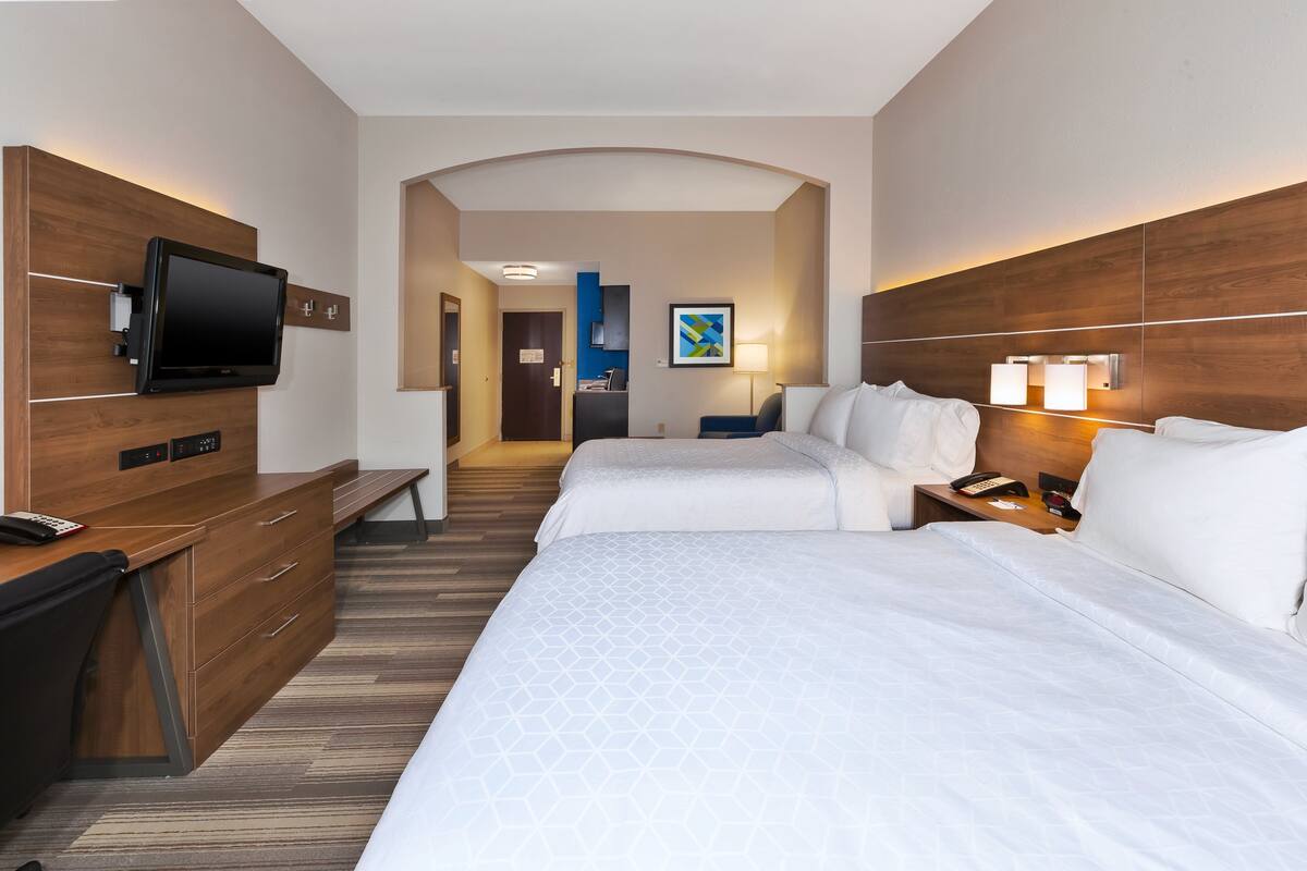 A hotel room with two beds, a desk with a TV, a lamp, and a phone on the nightstand.