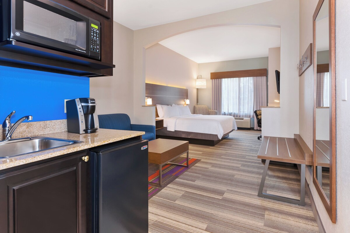 Une chambre d’hôtel équipée d’une kitchenette, d’un lit, d’un bureau, d’une chaise et d’un téléviseur.