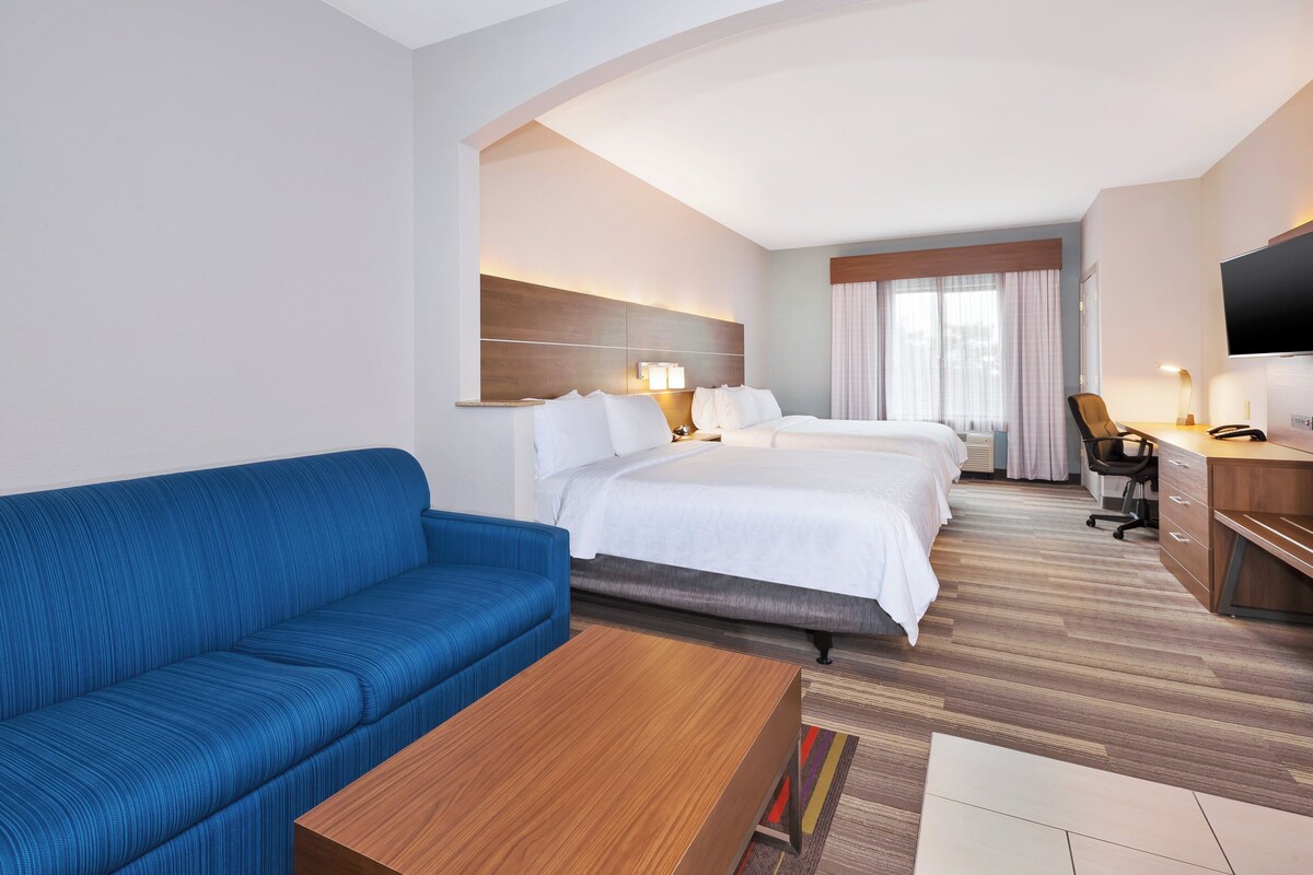Une chambre d’hôtel avec un canapé bleu, une table basse en bois, un lit avec une literie blanche, un bureau avec une chaise et un téléviseur fixé au mur.