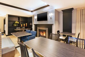 A modern living room with a fireplace, a flat-screen TV mounted above it, and a dining area with a long table and chairs. - Holiday Inn Express & Suites Warminster - Horsham by IHG (Warminster)