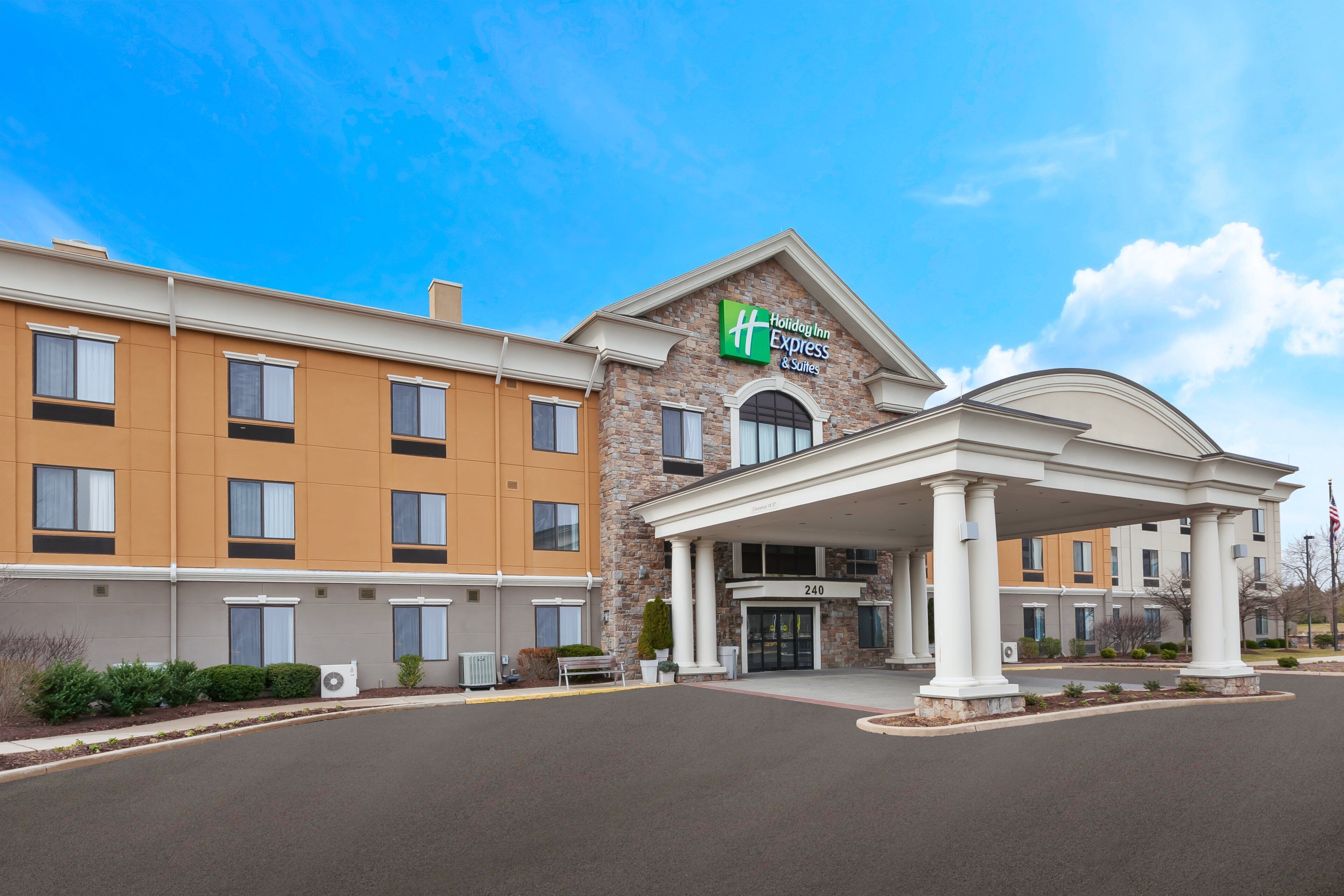 A Holiday Inn Express & Suites building with a brick facade, a covered entrance, and a clear blue sky.