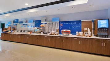 Um balcão de café da manhã moderno com diversas opções de comida, uma área de padaria e um bebedouro.
