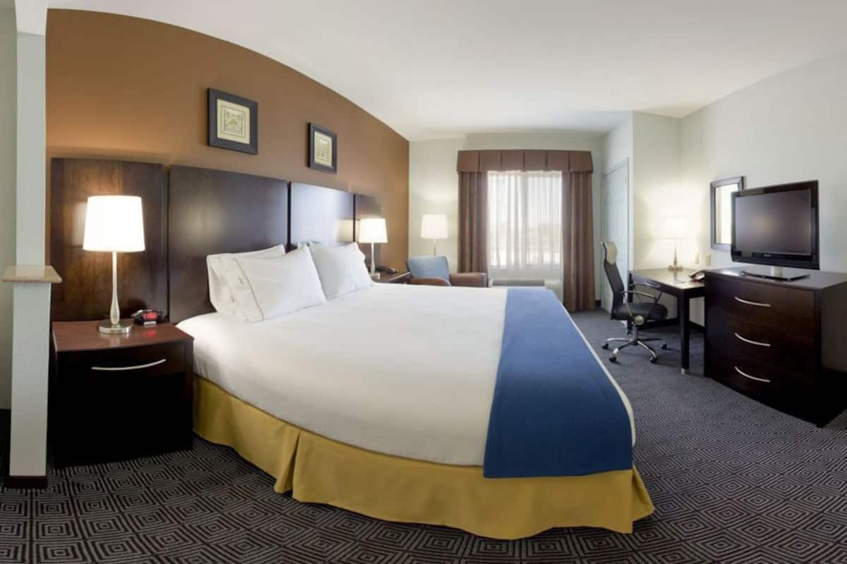 A hotel room with a large bed, a desk with a chair, a television, and a sofa.