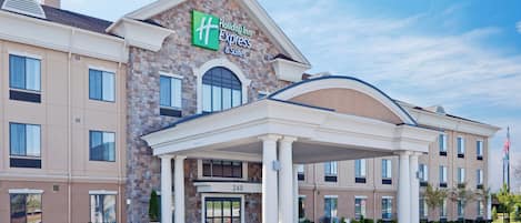 A Holiday Inn Express & Suites hotel with a stone facade, a covered entrance, and a clear sky.