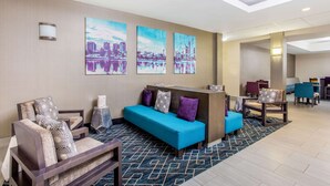 Un vestíbulo de hotel con recepción, zona de estar con sofás y sillones, y obras de arte en las paredes.