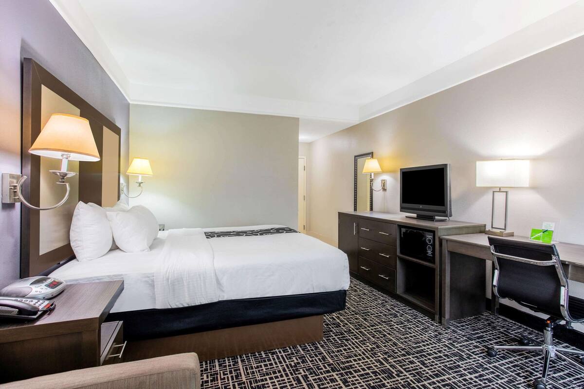 Ein Hotelzimmer mit Bett, Schreibtisch, Stuhl, Fernseher und Lampen.