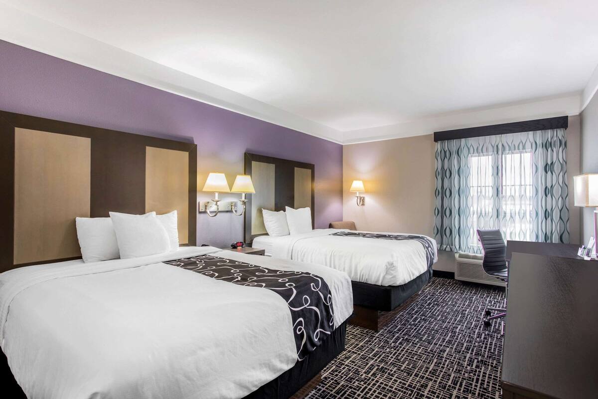 Ein Hotelzimmer mit zwei Betten, einem Schreibtisch und einem Fenster mit gemusterten Vorhängen.