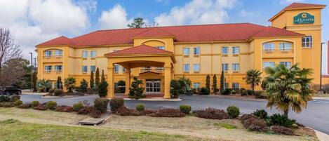 Un edificio giallo con tetto rosso, diverse finestre e un cartello con su scritto 'La Quinta Hotel & Suites'.