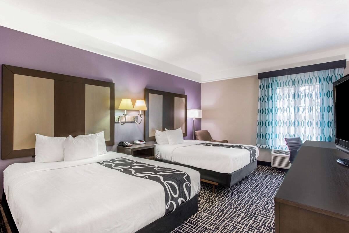Ein Hotelzimmer mit zwei Betten, einem Schreibtisch, einem Fernseher und einem Badezimmer.