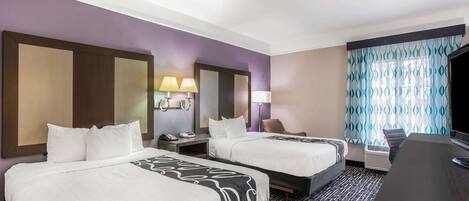 A hotel room with two beds, a desk, a TV, and a bathroom.