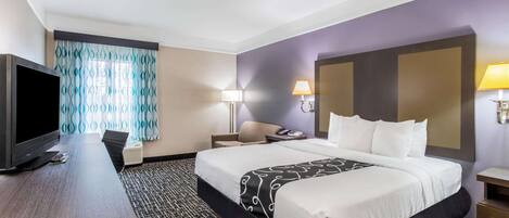 A hotel room with a large bed, a desk with a TV, two bedside lamps, and a patterned carpet.