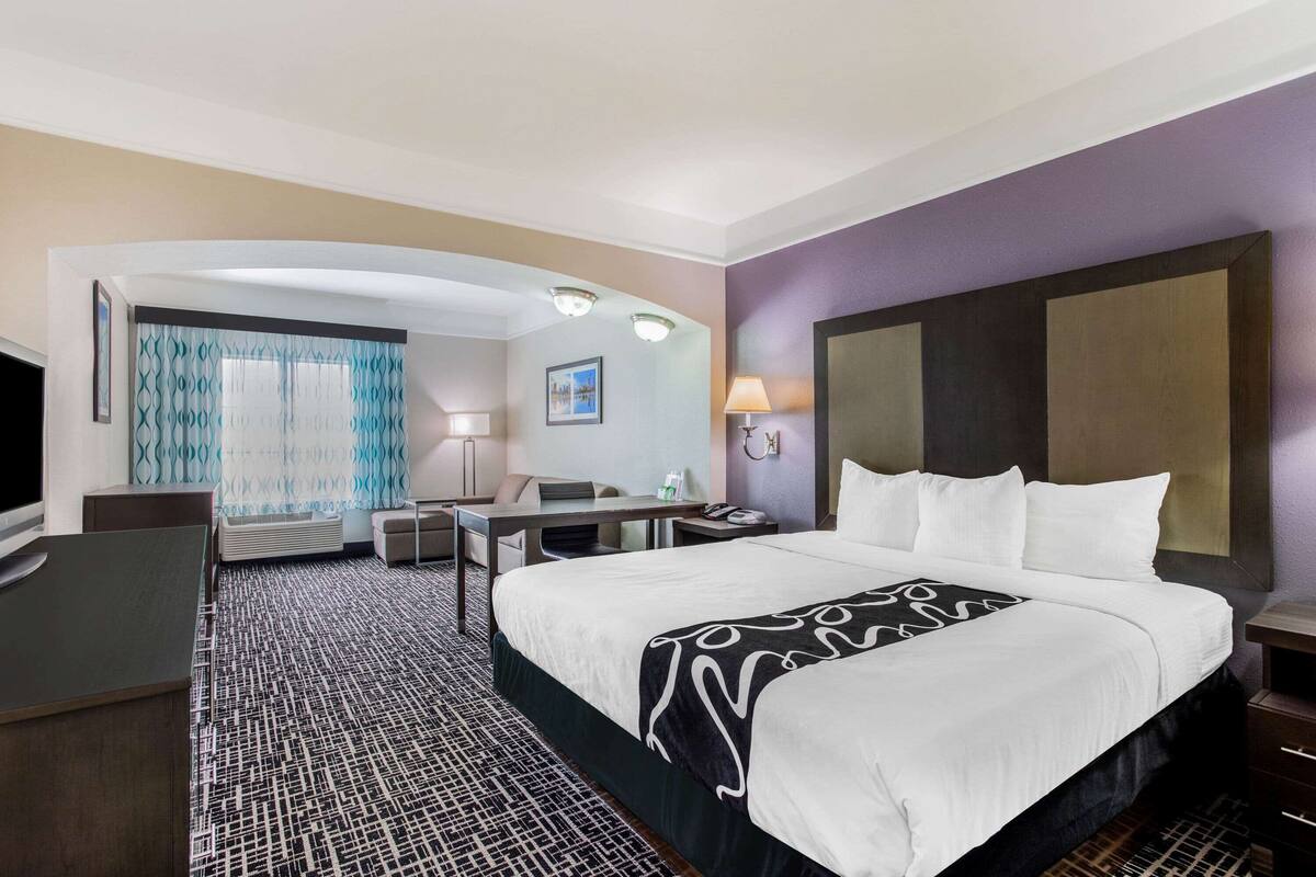 Ein Hotelzimmer mit einem großen Bett, einem Schreibtisch, einem Sessel, einem Fernseher und einem Badezimmer mit Dusche und WC.