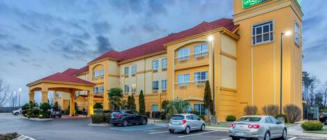 A hotel with a yellow facade, multiple balconies, and a parking lot with several cars.