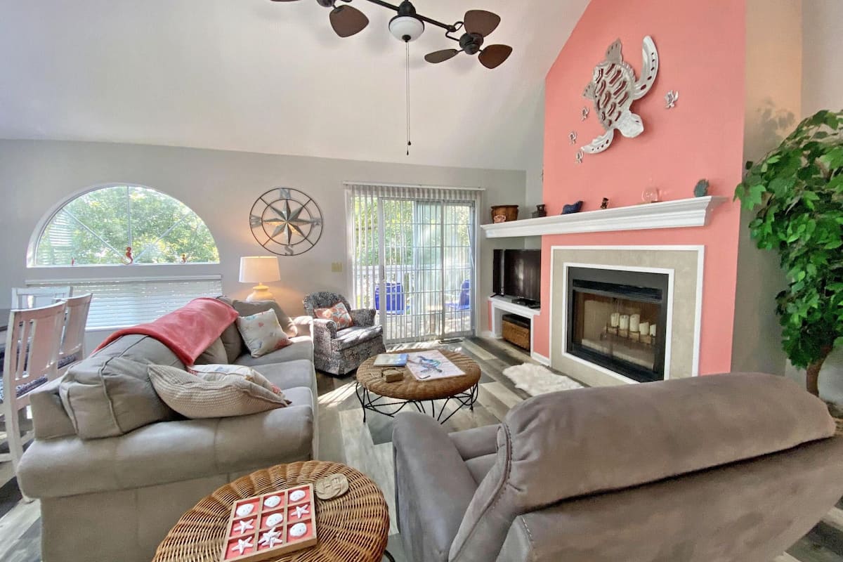 A living room with a fireplace, two sofas, a coffee table, and a ceiling fan.