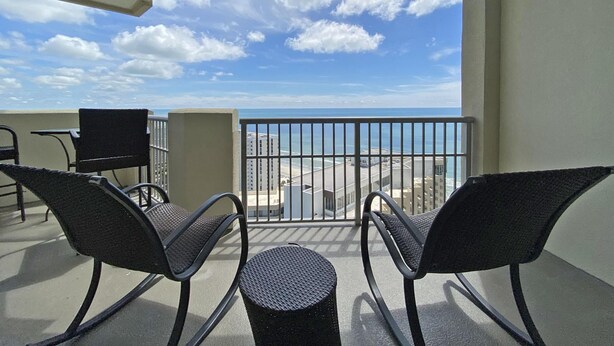 Ein Balkon mit zwei Stühlen und einem kleinen Tisch mit Blick auf einen Strand und das Meer.
