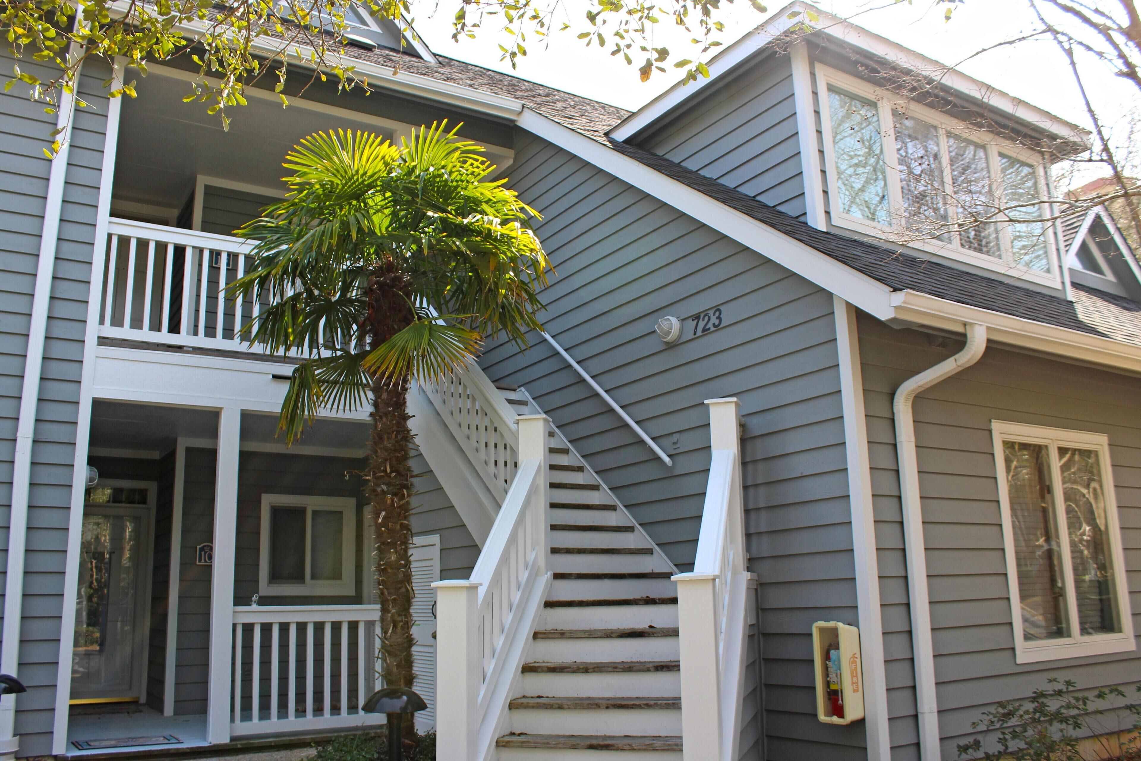 A two-story house with a front porch, a staircase, and a palm tree.