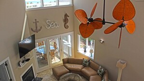 Ein Wohnzimmer mit einem großen Ecksofa, einem Flachbildfernseher, einem Kamin und einem Deckenventilator.