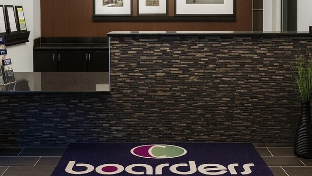 A reception area with a welcome sign, framed pictures, a reception desk, and a logo for boarders inn & suites by Eopeteglogo. - Boarders Inn & Suites by Cobblestone Hotels – Ashland City (Ashland City)