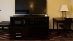 A hotel room with a flat-screen TV on a cabinet, a desk with a lamp, a chair, and a microwave. - Boarders Inn & Suites by Cobblestone Hotels – Ashland City (Ashland City)