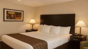 A hotel room with a large bed, two bedside tables with lamps, a framed artwork on the wall, and a green chair. - Boarders Inn & Suites by Cobblestone Hotels – Ashland City (Ashland City)