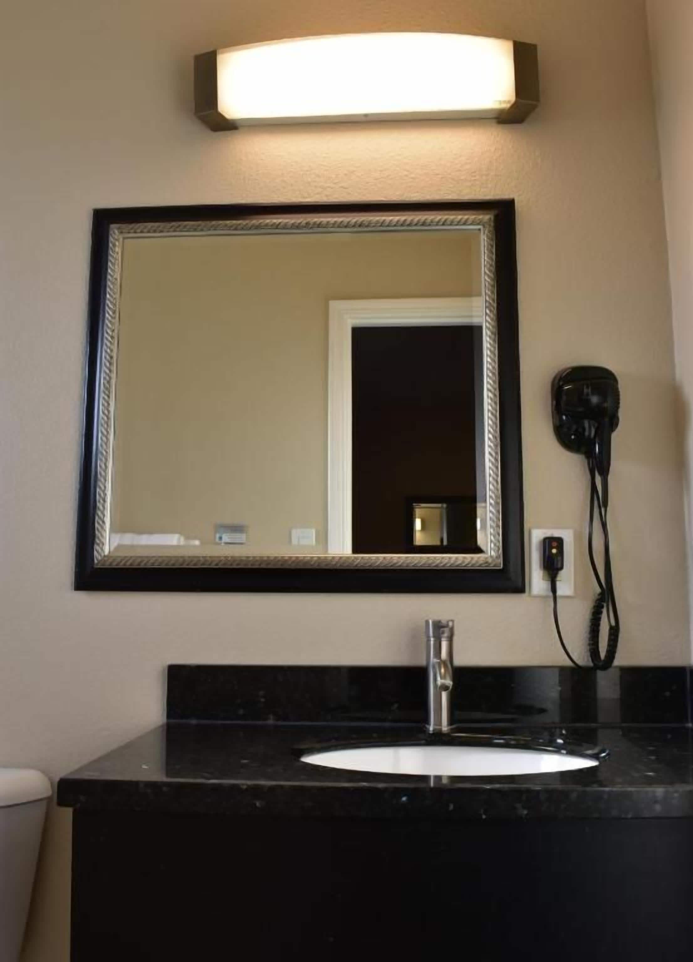 A bathroom with a black countertop, a white sink, a mirror with a black frame, and a hairdryer plugged in.