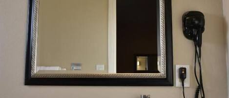 A bathroom with a black countertop, a white sink, a mirror with a black frame, and a hairdryer plugged in.