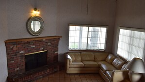 Sala de estar com lareira de tijolos, sofá de couro, luminária e janela com persianas.