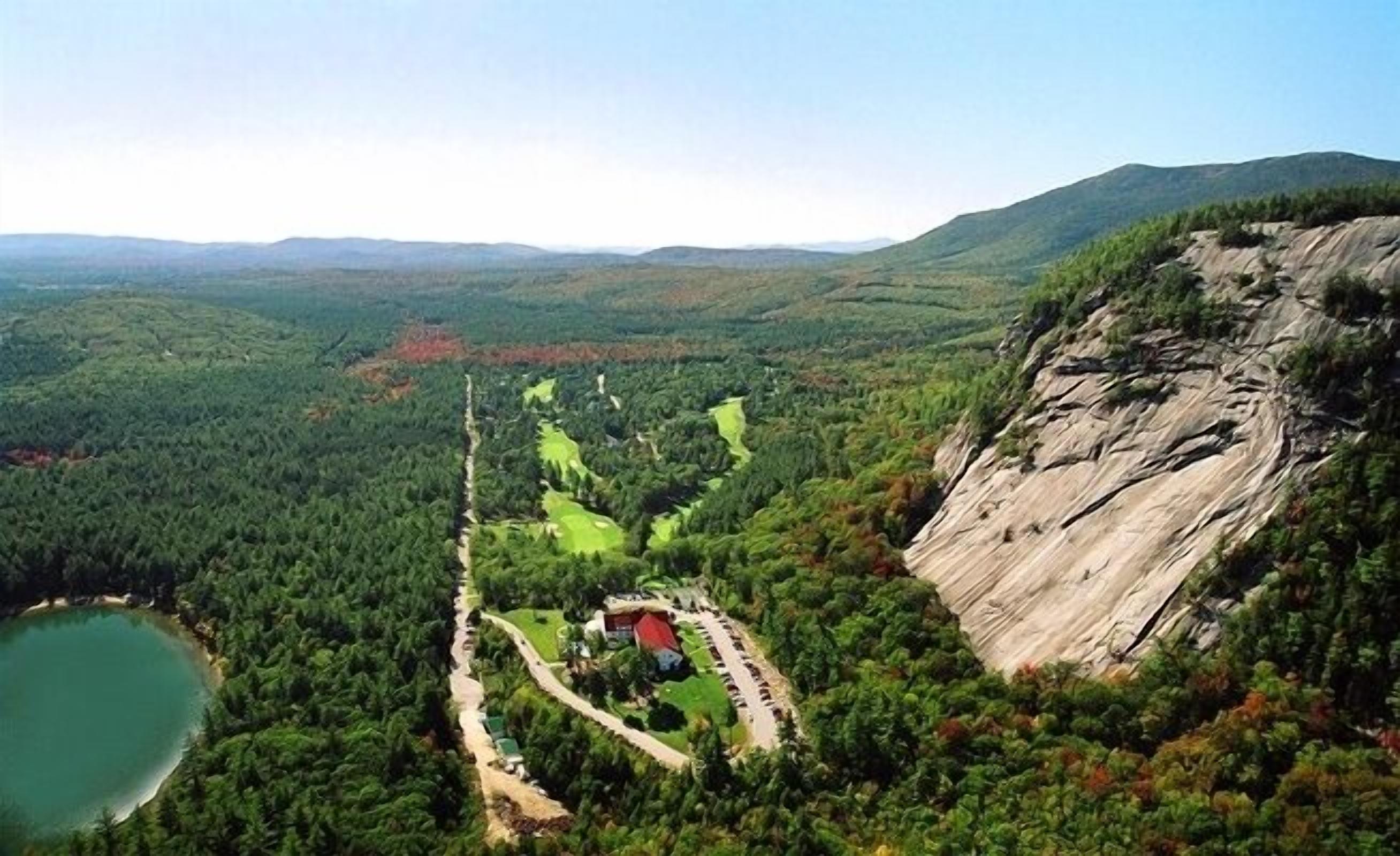 A mountainous landscape with a lake, a winding road, and a building with a red roof.