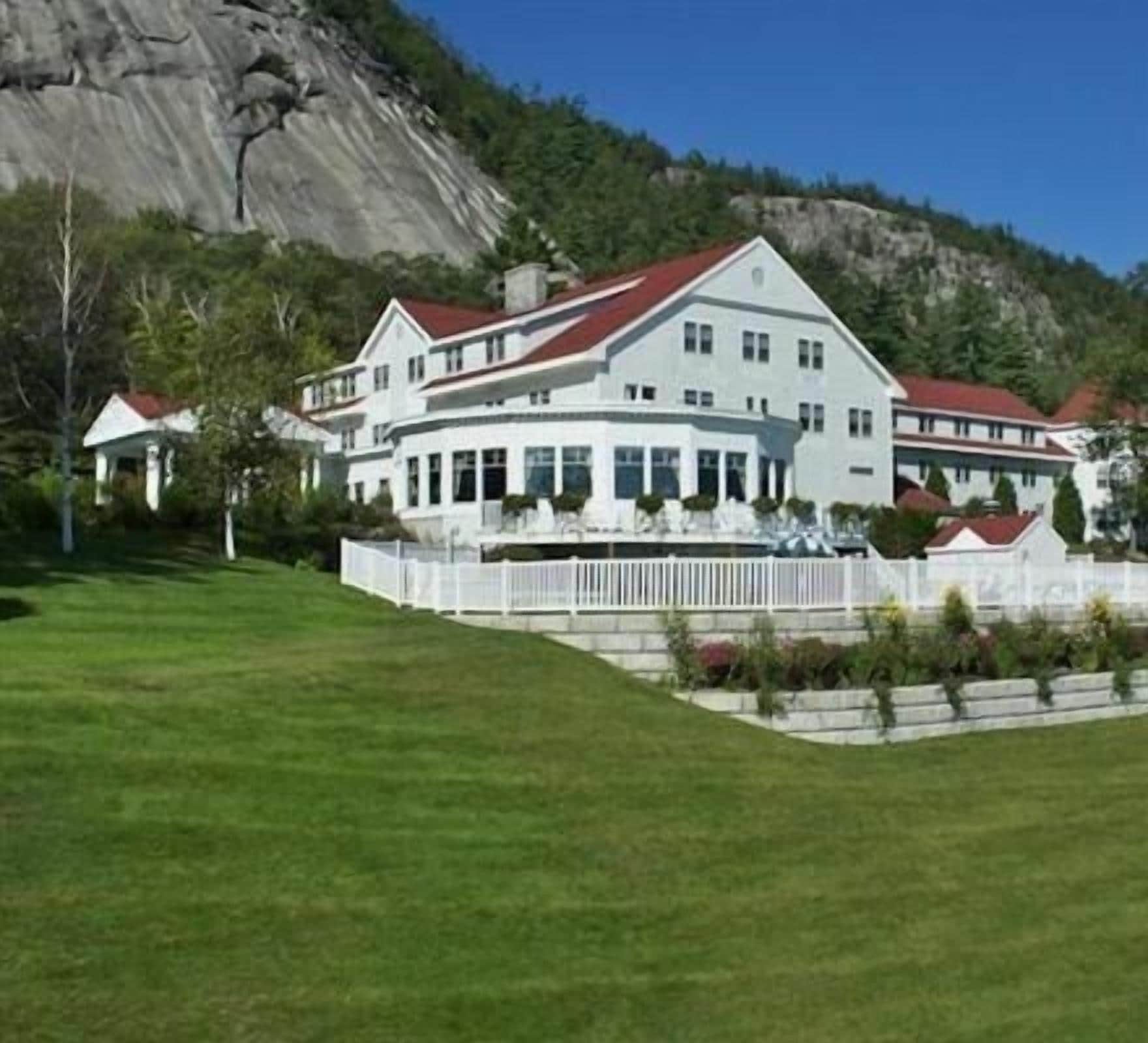 A large, multi-story building with a red roof, surrounded by a white fence and lush green lawn.