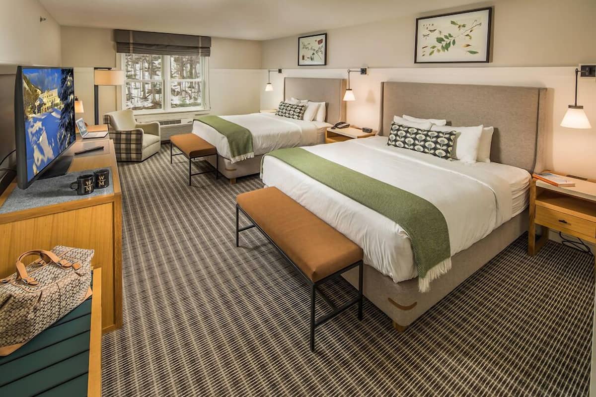 Une chambre d’hôtel avec deux lits, un bureau avec une télévision, un banc et une fenêtre donnant sur des arbres.
