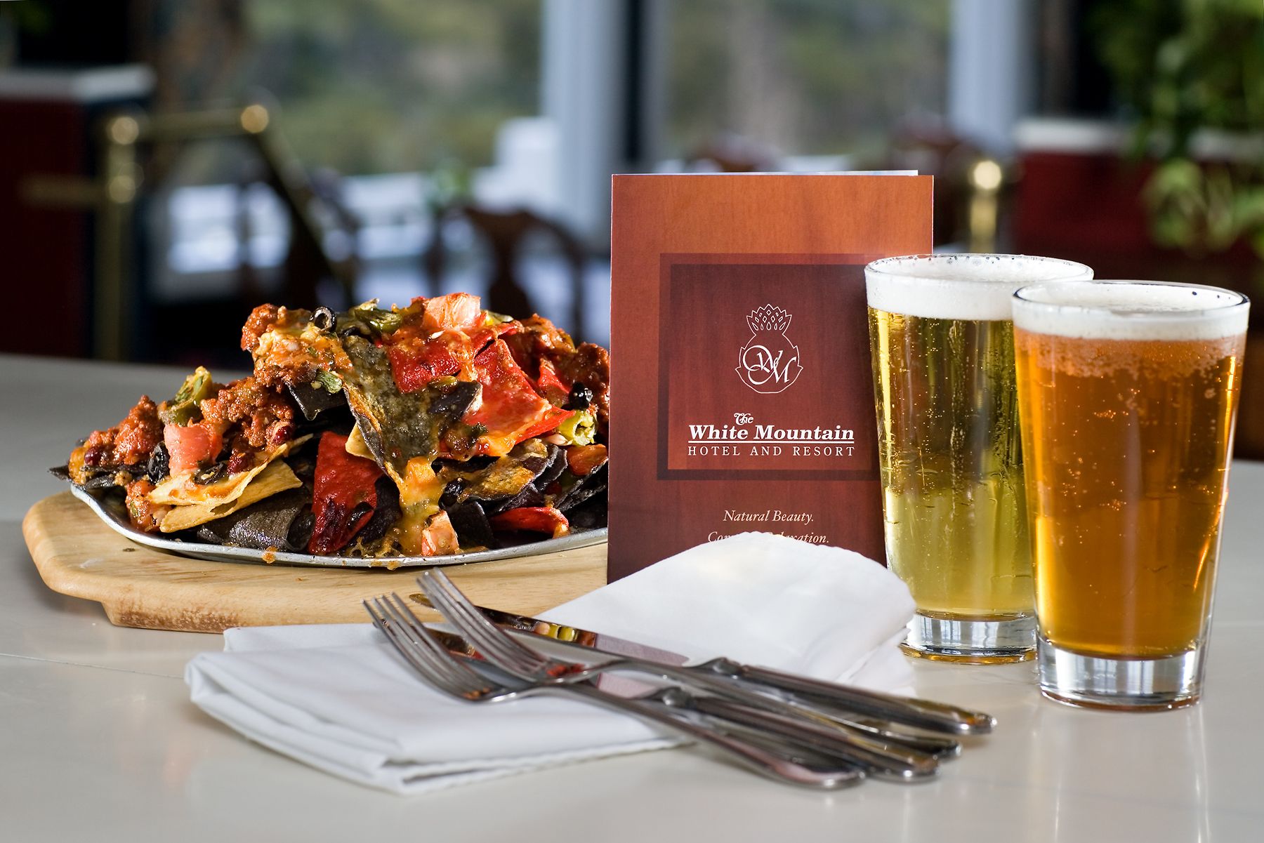 A plate of nachos, two glasses of beer, and a menu from The White Mountain Hotel and Resort.