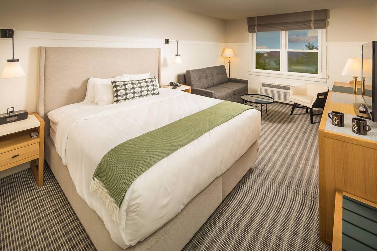 Une chambre d’hôtel avec un grand lit, un bureau, une chaise, un canapé, une petite table et une fenêtre donnant sur un beau paysage.