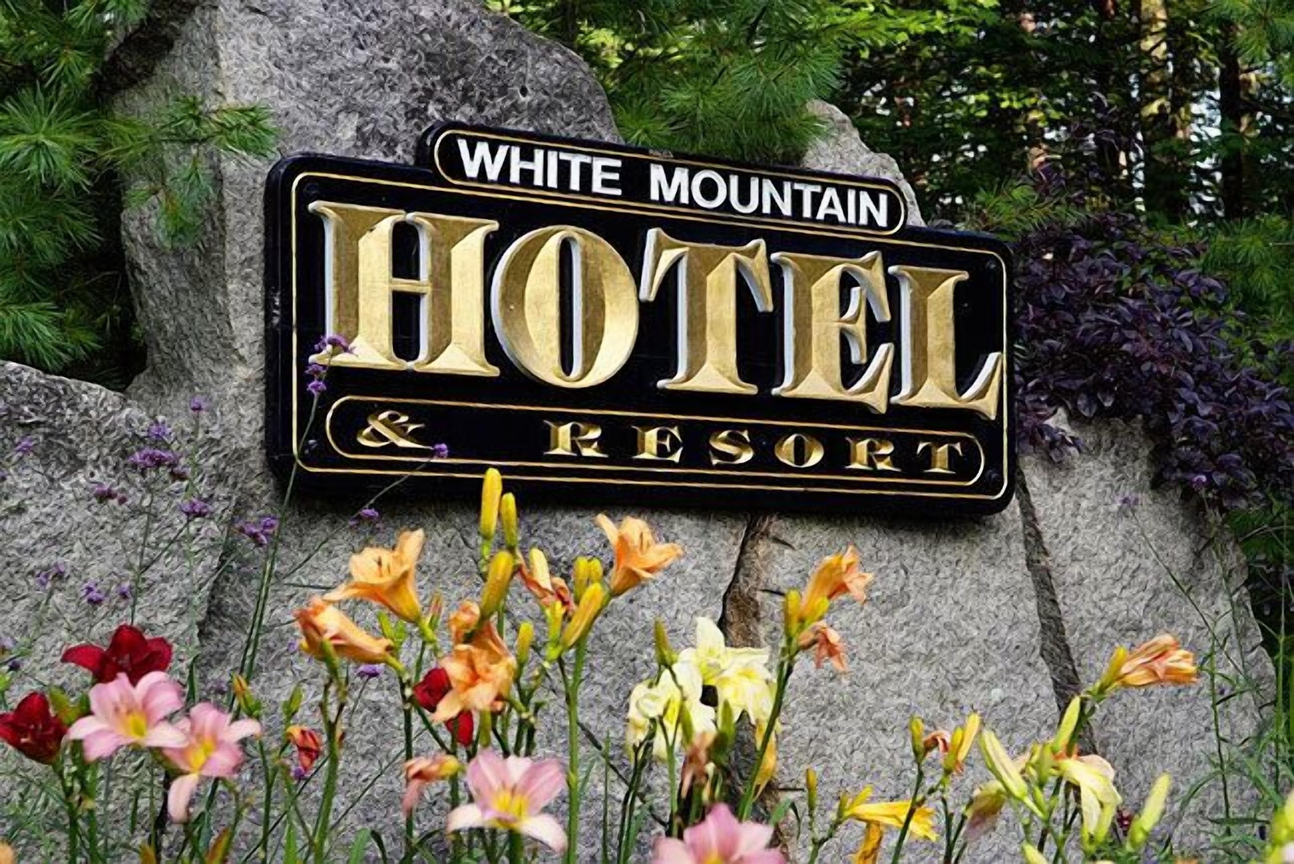 A sign for White Mountain Hotel & Resort with a stone background and flowers in the foreground.
