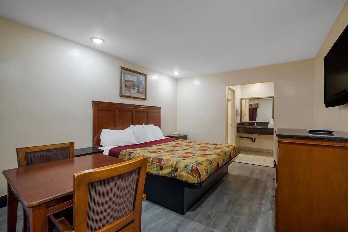 A hotel room with a bed, a desk, a chair, a television, and a bathroom visible through an open door.