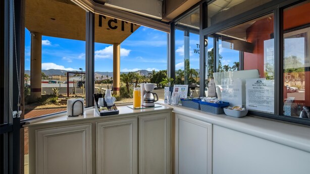 Un bar pour prendre le petit-déjeuner avec vue sur les montagnes et les palmiers, une machine à café et des aliments pour le petit-déjeuner disposés sur le comptoir.