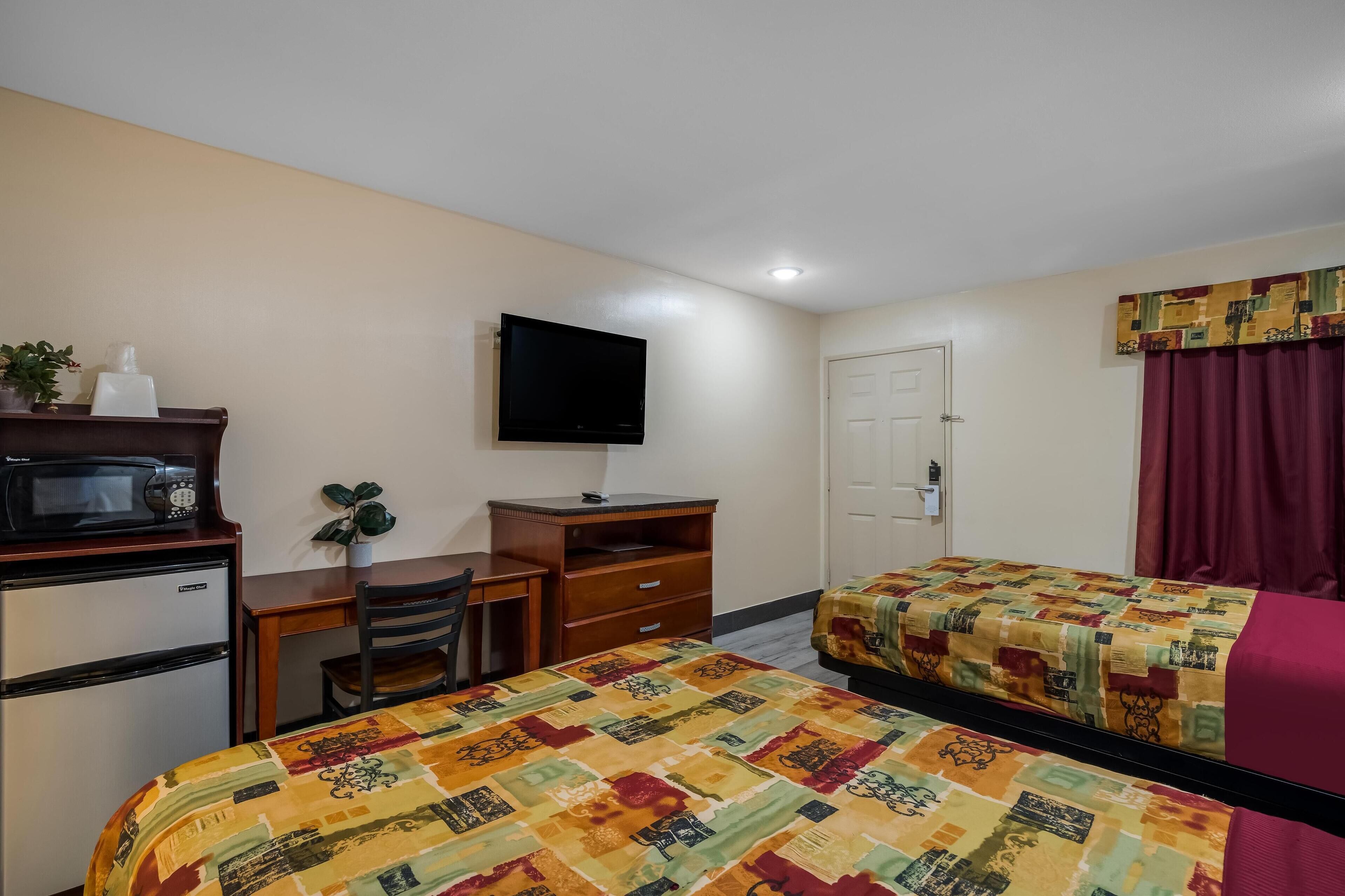 A hotel room with two beds, a desk, a chair, a television, a microwave, and a refrigerator.