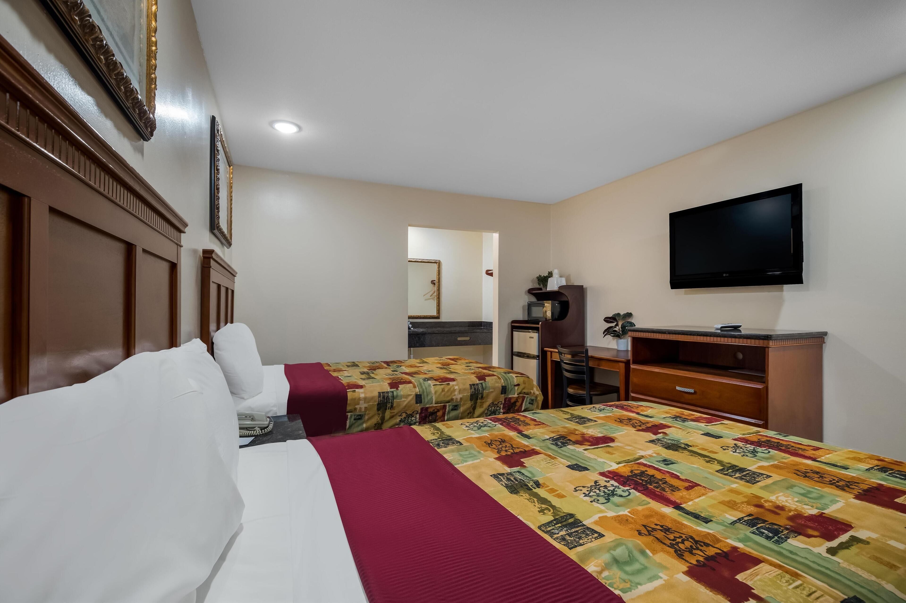 Una habitación de hotel con dos camas, televisión, escritorio y espejo.