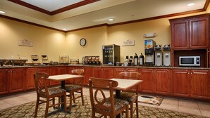 A hotel breakfast area with wooden cabinets, a clock, a coffee machine, and a microwave.
