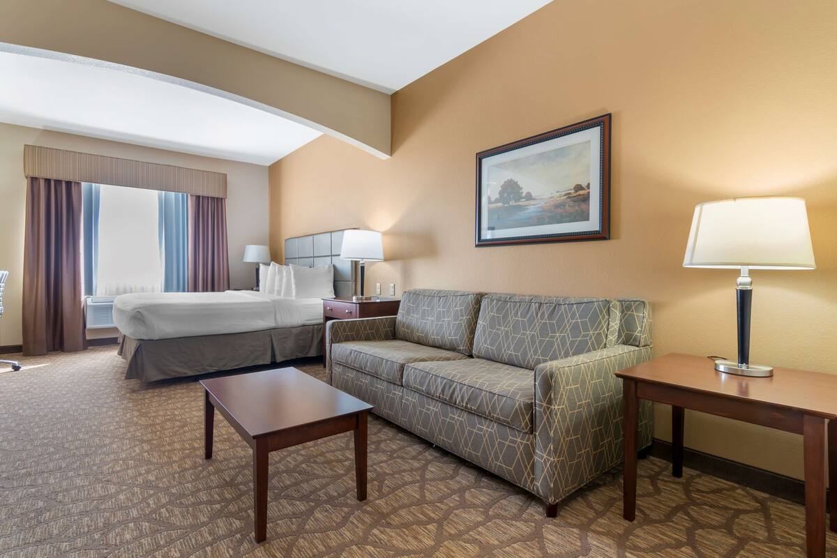 A hotel room with a bed, a sofa, a small table, a lamp, and a framed picture on the wall.