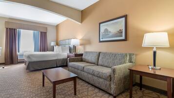 A hotel room with a bed, a sofa, a small table, a lamp, and a framed picture on the wall.