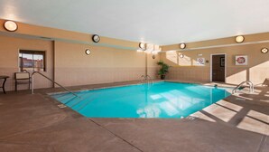 An indoor swimming pool with clear water, surrounded by beige walls and a tiled floor.