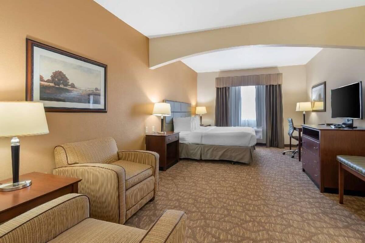 A hotel room with a bed, two bedside tables with lamps, a desk with a chair, a television, and a framed picture on the wall.
