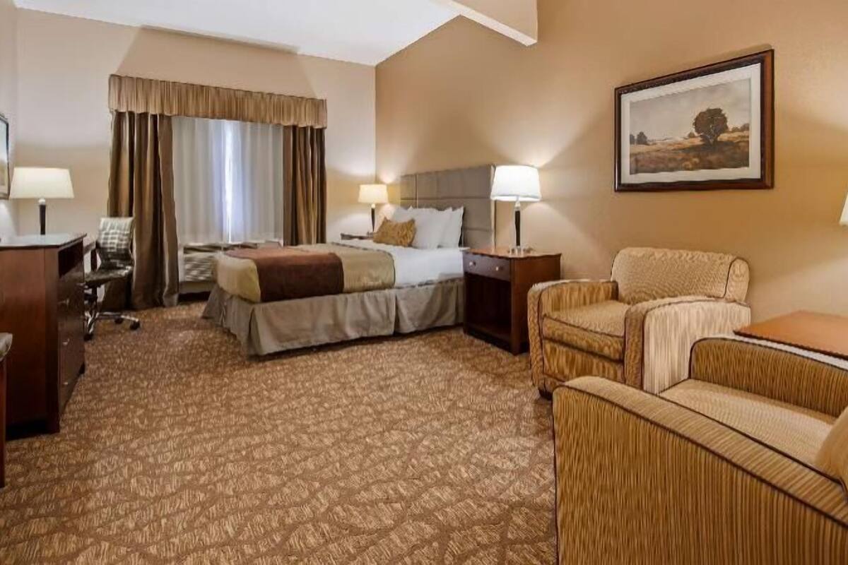 A hotel room with a bed, two bedside tables with lamps, a chair, a desk, and a painting on the wall.