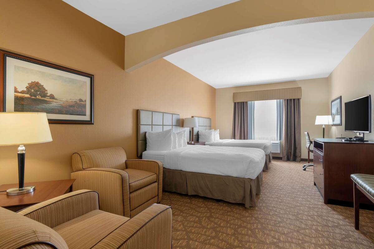 A hotel room with two beds, a desk, a chair, a TV, and a painting on the wall.