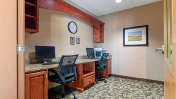 A conference room with two desks, chairs, a clock, and framed certificates on the wall.
