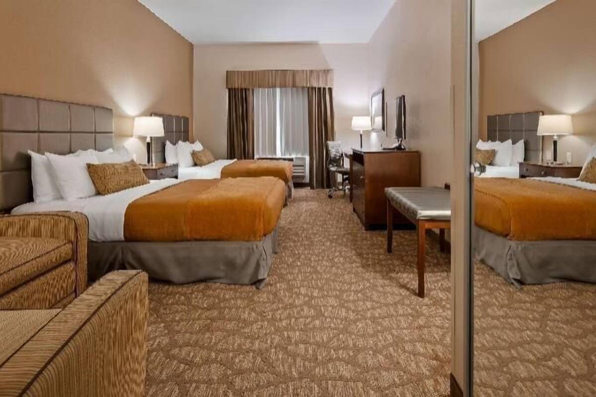 A hotel room with two beds, a desk, a chair, and a small sofa.